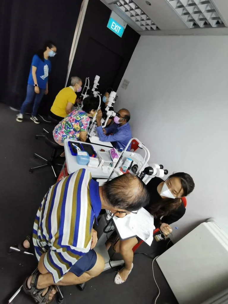 Senior resident undergoing an eye screening test with volunteer nurses assisting